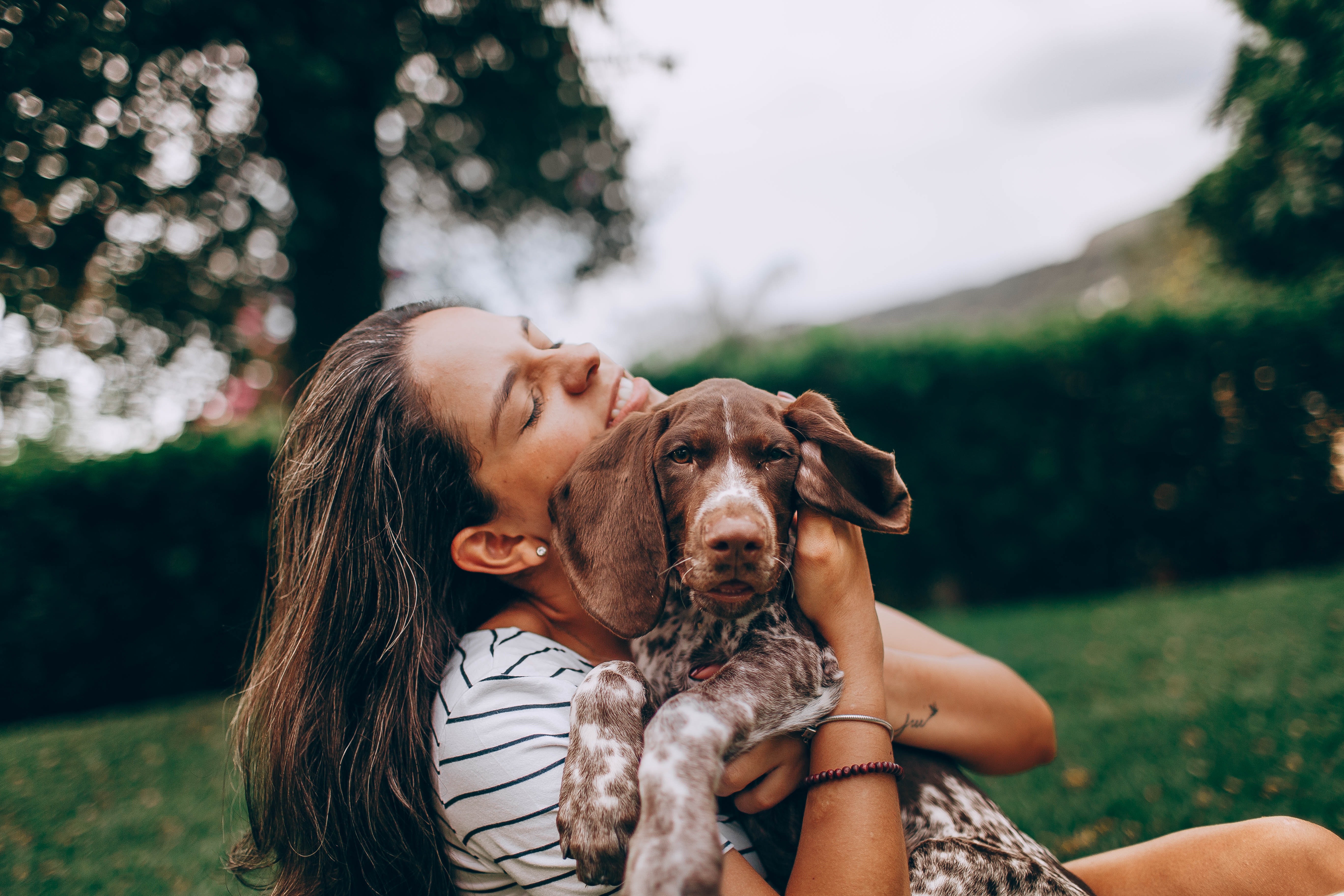 woman in white and black stripe top hugging a dog